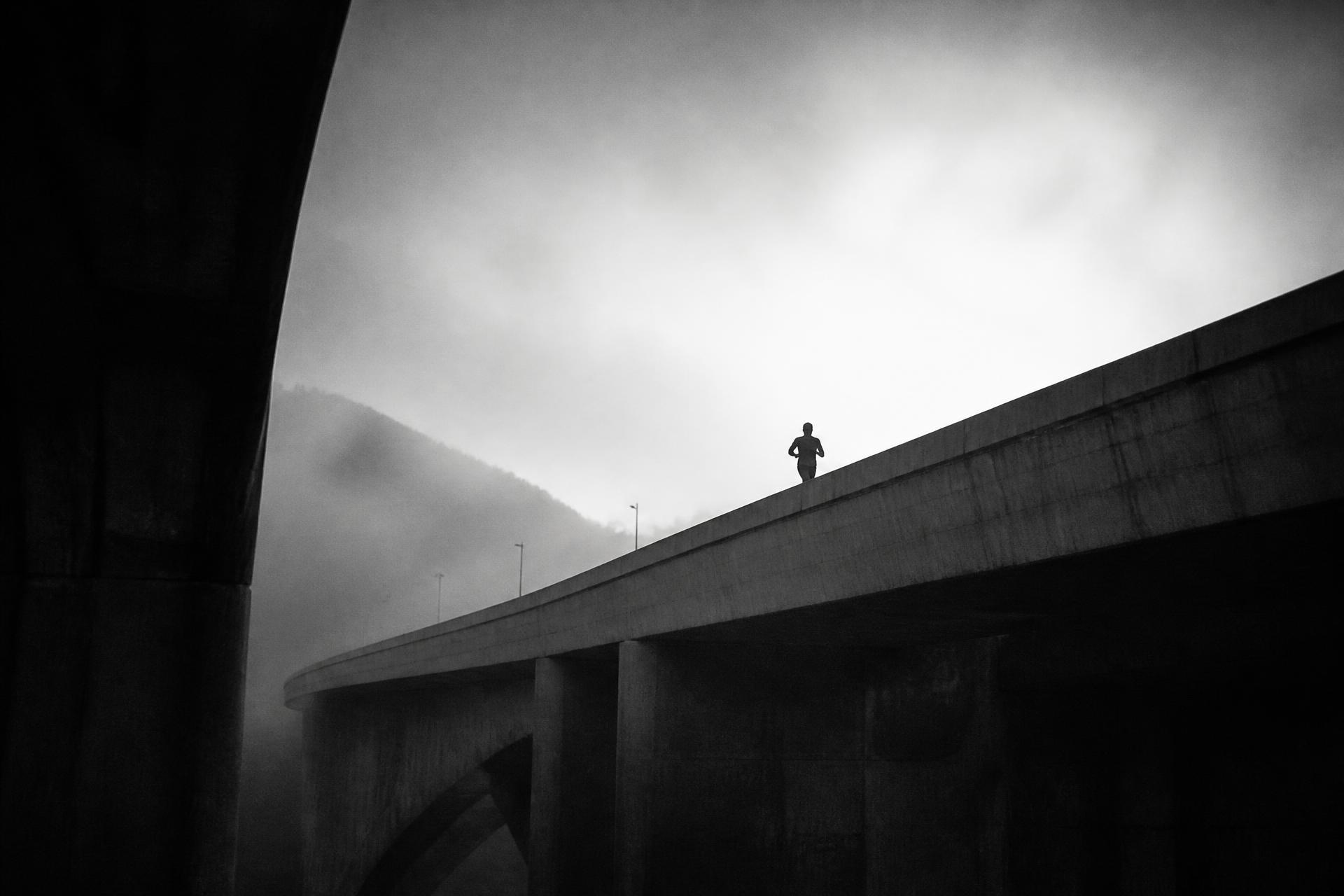 A lone runner crossing a fog-covered concrete overpass at dawn